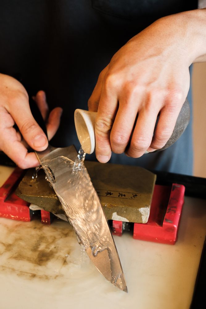 Water wordt op een wetsteen gegoten tijdens het handmatig slijpen van een keukenmes